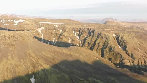 fotografía de un avión no tripulado del cañón de klfurárgil en islandia, con acantilados escarpados, tierras altas verdes y montañas cubiertas de nieve bajo un cielo despejado