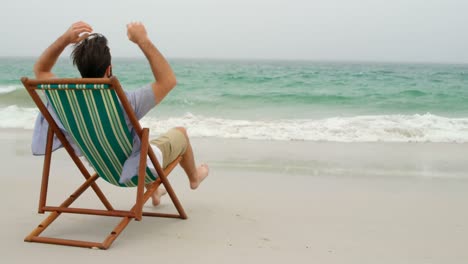 Rear-view-of-man-relaxing-with-hands-behind-head-on-sun-lounger-at-beach-4k