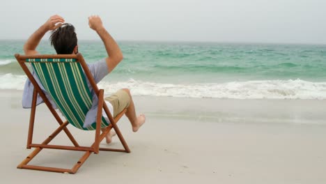 Vista-Trasera-Del-Hombre-Relajándose-Con-Las-Manos-Detrás-De-La-Cabeza-En-Una-Tumbona-En-La-Playa-4k