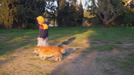 Toma-Panorámica-De-Un-Niño-Caucásico,-Caminando-Con-Su-Perro-Mascota-Con-Una-Correa,-En-Los-Campos-Cerca-Del-Bosque-De-Parnitha,-Atenas,-Grecia