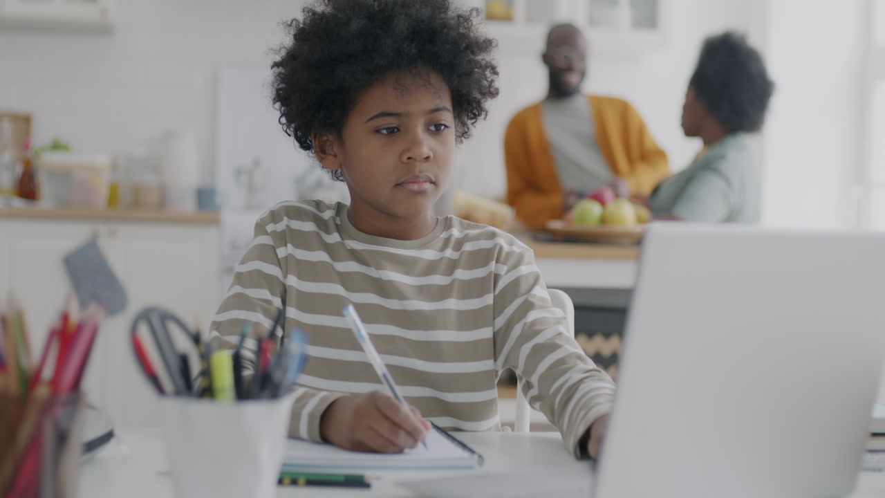 Child doing homework at home with family in kitchen