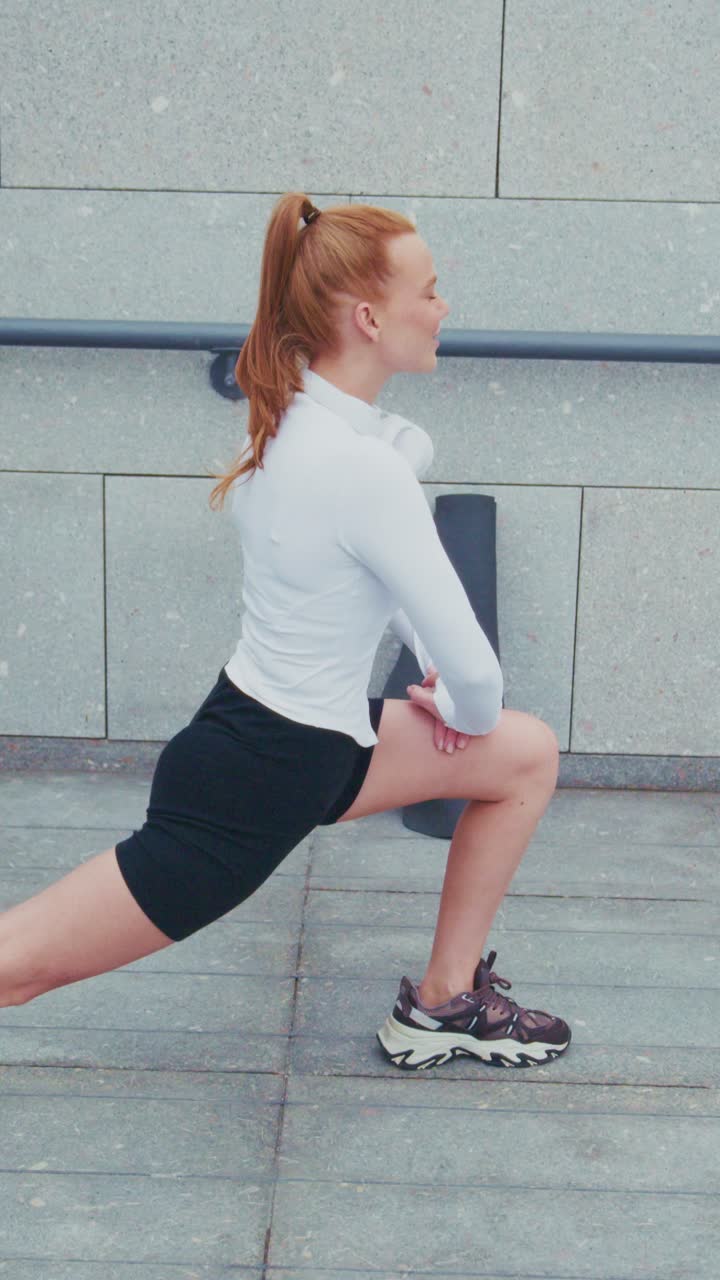 Eine engagierte Fitness-Enthusiastin führt eine dynamische Dehnroutine aus, zeigt Eleganz und Stärke durch Ausfallschritte in urbaner Umgebung.