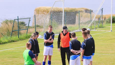 male and female soccer players listening to male coach giving instructions on pitch