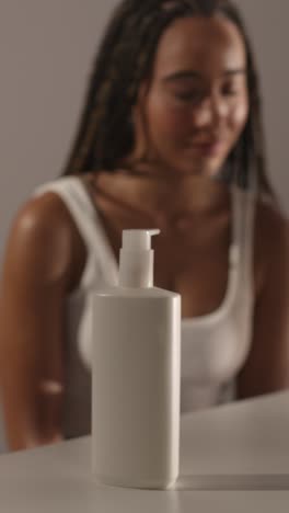 studio skincare beauty shot of woman with moisturiser bottle in foreground