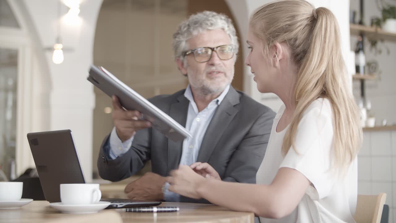 Focused Caucasian businessman holding clipboard and showing to blond woman