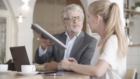 focused caucasian businessman holding clipboard and showing to blond woman