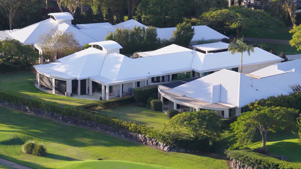 Drone captures luxurious homes with white roofs surrounded by greenery in Gold Coast, Australia. Bright daylight enhances the serene atmosphere