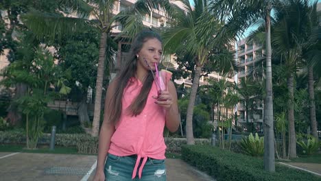 niña bebiendo bebida contra las palmeras verdes en un día de viento caliente