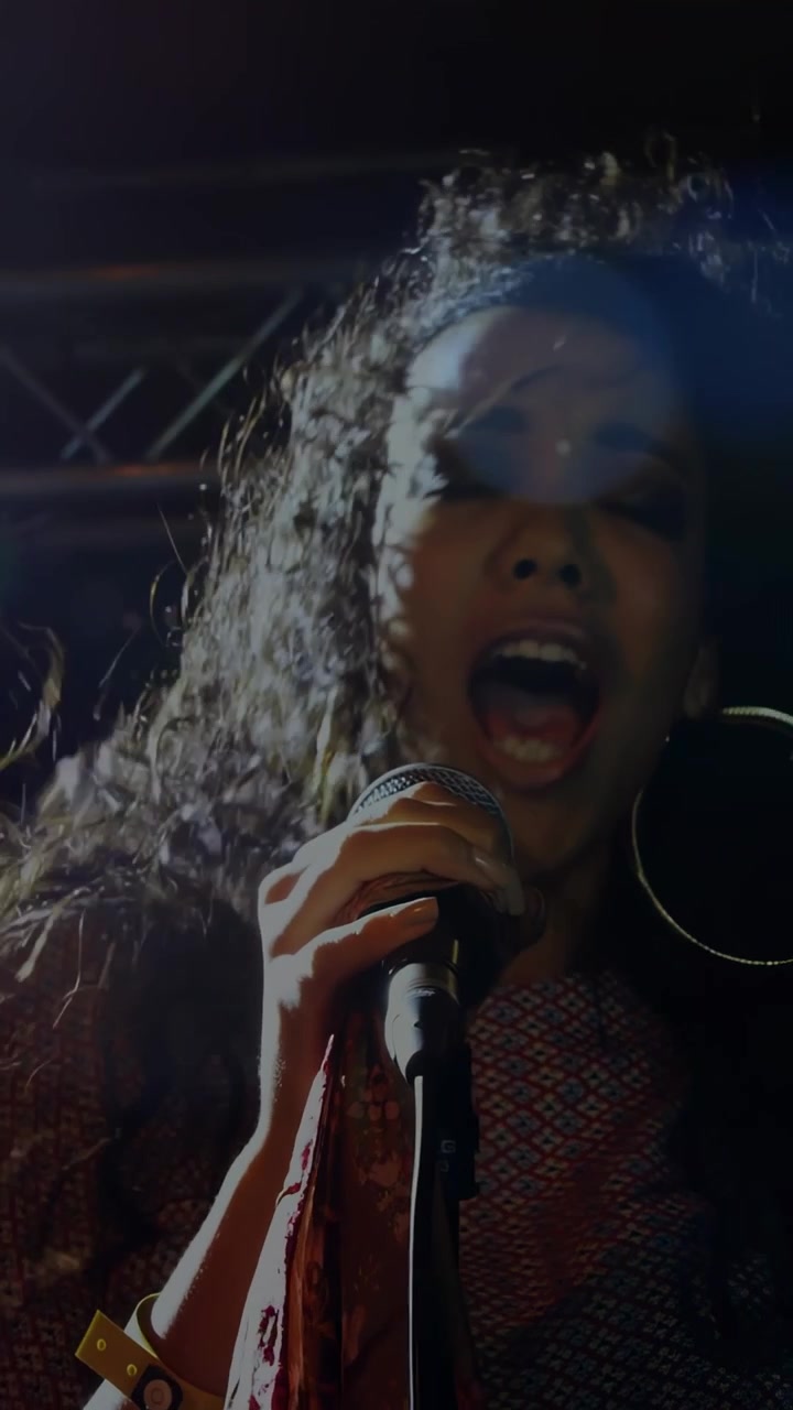 Vertical video: Female singer opening mouth, singing into mic on stage, hair whipping for audience