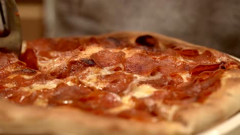 cutting fresh hot homemade pepperoni pizza into slices - isolated close up of the pizza wheel