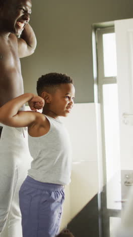 vertical video of happy african american father and son showing muscles to mirror