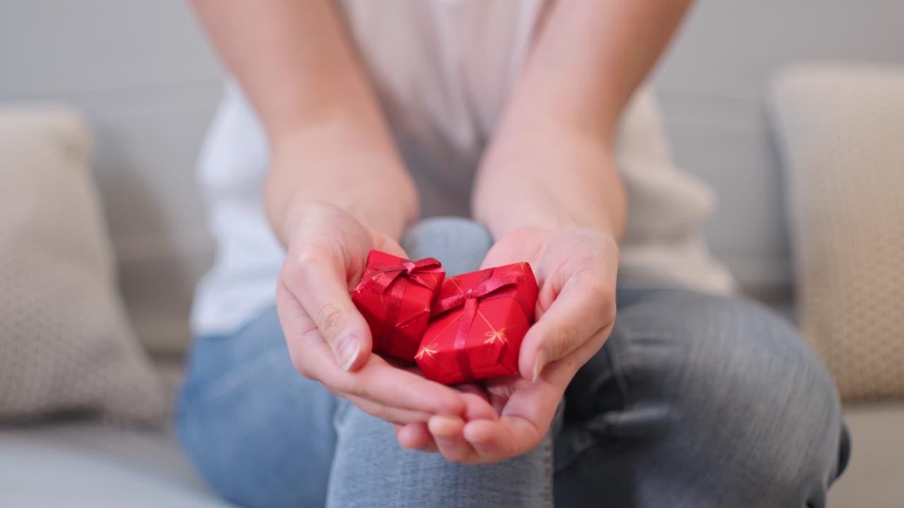Woman sitting on couch, showing Christmas decorations in form of small gifts. Static