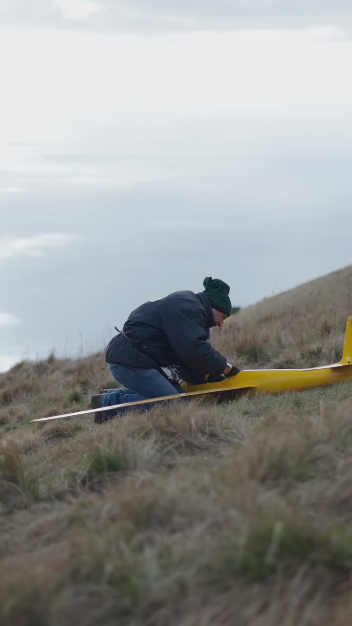 Man assembling a yellow glider on a grassy hill