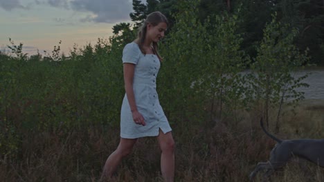 medium view of attractive young woman walking with her dog out of heather field in sand dunes