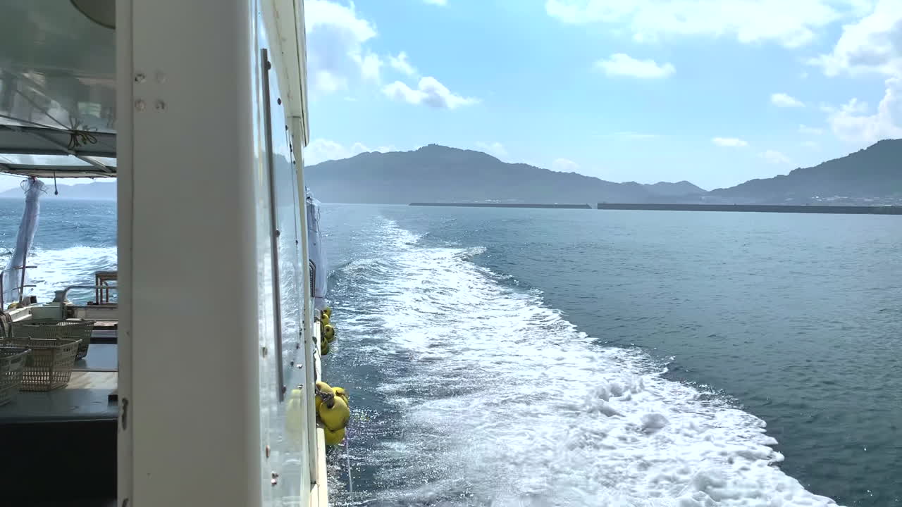 Motor boat sailing at full speed in the ocean leaving a trail of white foam as it moves away from the coast on a beautiful sunny day with mountains and the beach in the background rear view shot
