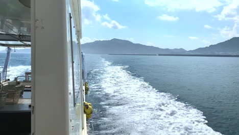 motor boat sailing at full speed in the ocean leaving a trail of white foam as it moves away from the coast on a beautiful sunny day with mountains and the beach in the background rear view shot
