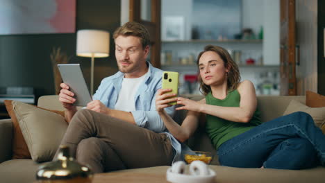 Love-partners-using-gadgets-at-cozy-house.-Woman-showing-mobile-phone-to-husband