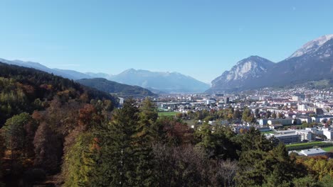 Innsbruck-in-daytime-aerial-view-going-away-on-a-hill-in-an-old-alpine-forest-in-autumn-with-calm-and-joyful-moment-with-the-alps-in-Tyrol-in-Austria-in-the-background