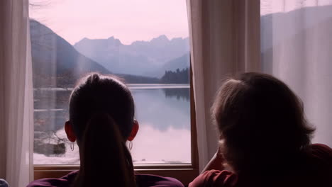 people looking out a window at a tranquil mountain lake