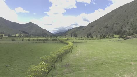 Dolly-out-mountainous-landscape,-vast-green-meadows,-wooden-borders-and-a-small-farm-house,-on-the-grass-the-shadow-of-the-clouds-is-reflected-while-the-wind-moves-them