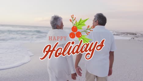 Animation-of-happy-holidays-text-over-happy-senior-biracial-couple-walking-on-beach-at-christmas