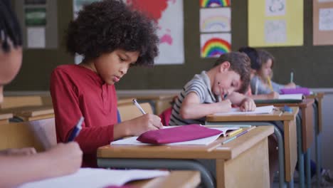 grupo de niños escribiendo mientras están sentados en su escritorio en clase en la escuela