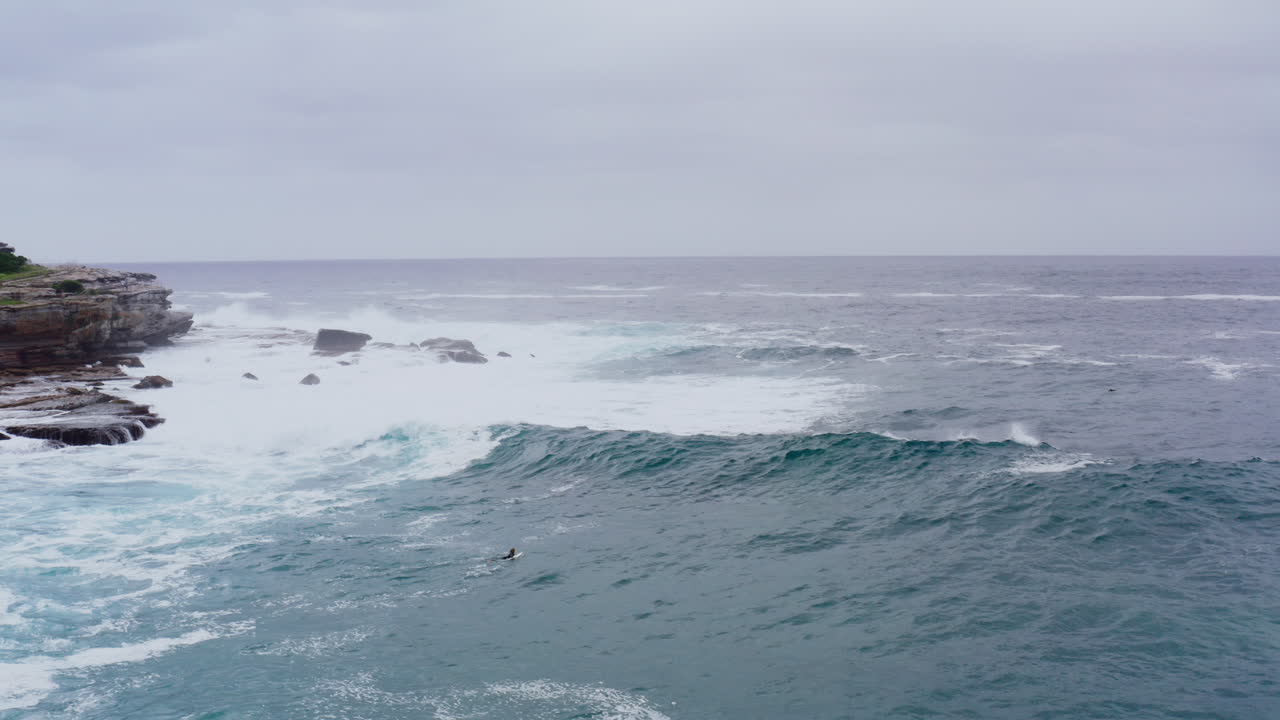 Aerial: A surfer paddles into big swell off Buckler at Bondi Beach, Sydney Australia