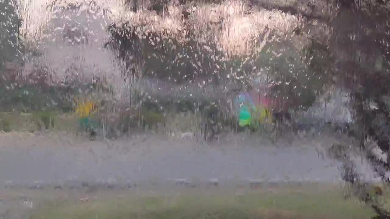 Agua escurriendo por una ventana de cristal, con gotas abstractas y un fondo suavemente desenfocado.