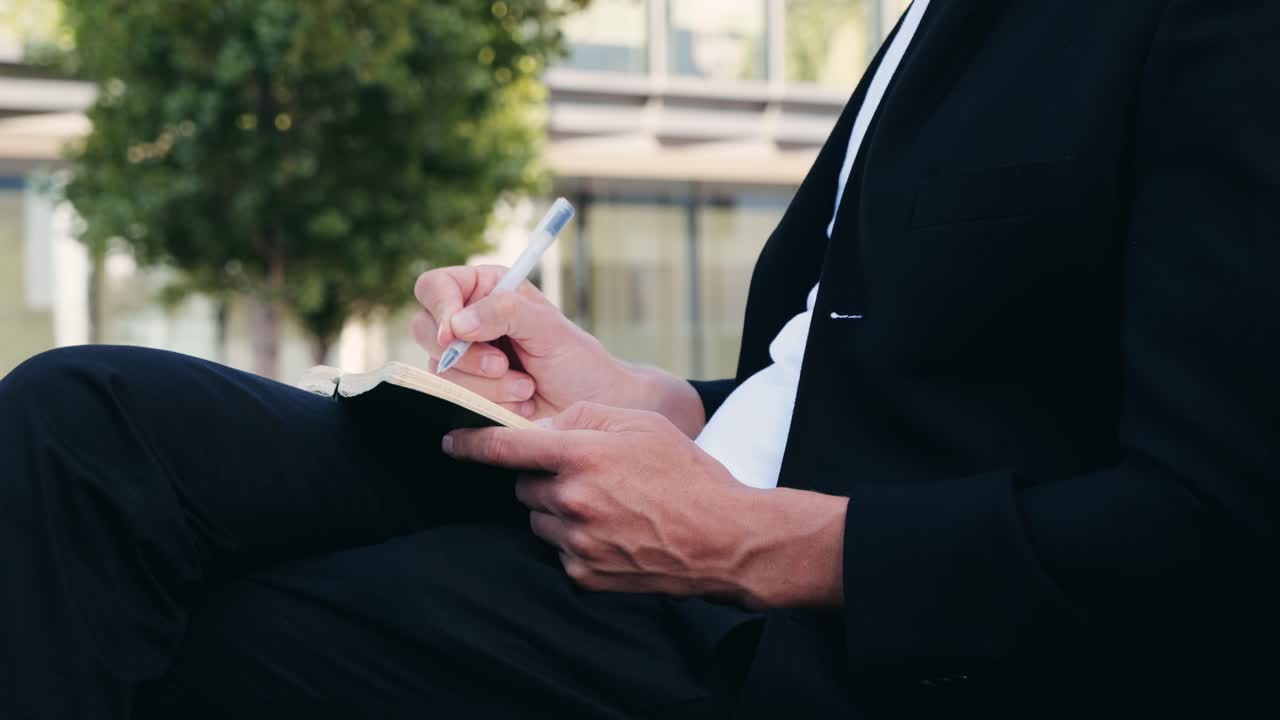 Man in suit writing in notebook outdoors