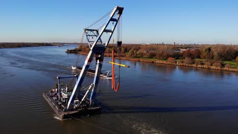 tugboat and floating sheerleg navigating the river with vast riverside landscape in barendrecht, netherlands