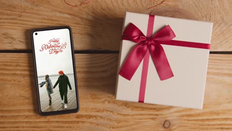 close up of hand putting valentine's day gift next to mobile phone with valentines message on screen