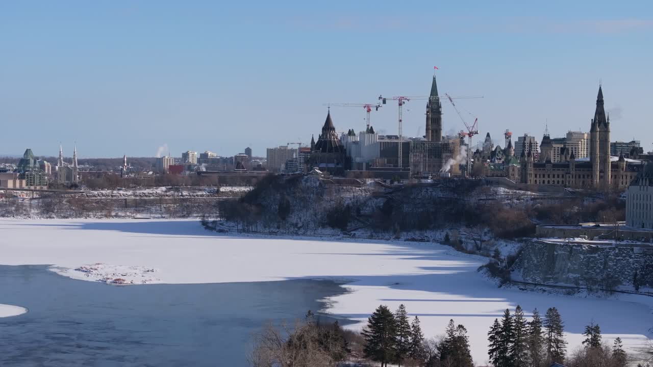 Long lens shot of Parliament Hill's Centre Block under renovation with cranes visible above the snowy Ottawa River cliffs