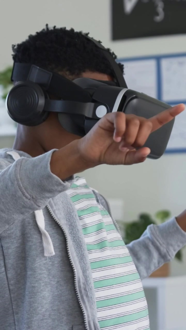 Studerende i stribet T-shirt og grå hættetrøje bruger VR-headset med hovedtelefoner i et klasseværelse med en matematik-tavle.