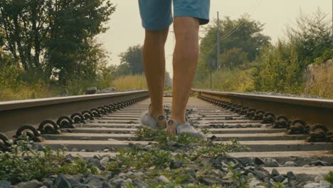 detail of feet walking inside the tracks, man turns away and proceeds inside the tracks on a hot summer day