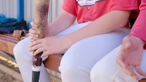 a youth baseball team is seated on the bench equipped with bats and gloves in hand