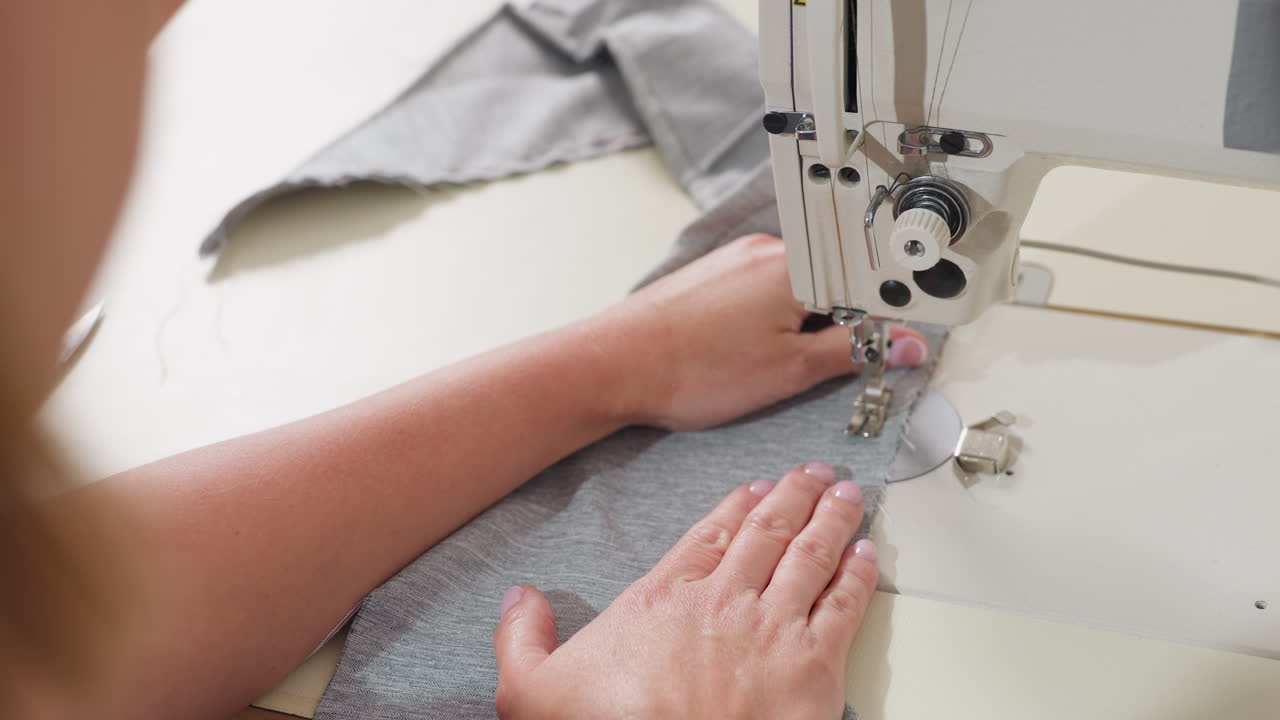 Garment maker slides cloth into needle on electronic machine, ensuring alignment, focusing on careful sewing technique, guiding fabric with skill, demonstrating professional quality