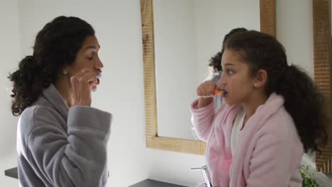 Happy-mixed-race-mother-and-daughter-brushing-teeth-in-bathroom