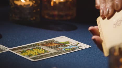 close up of woman giving tarot card reading on candlelit table holding card showing heart pierced by swords