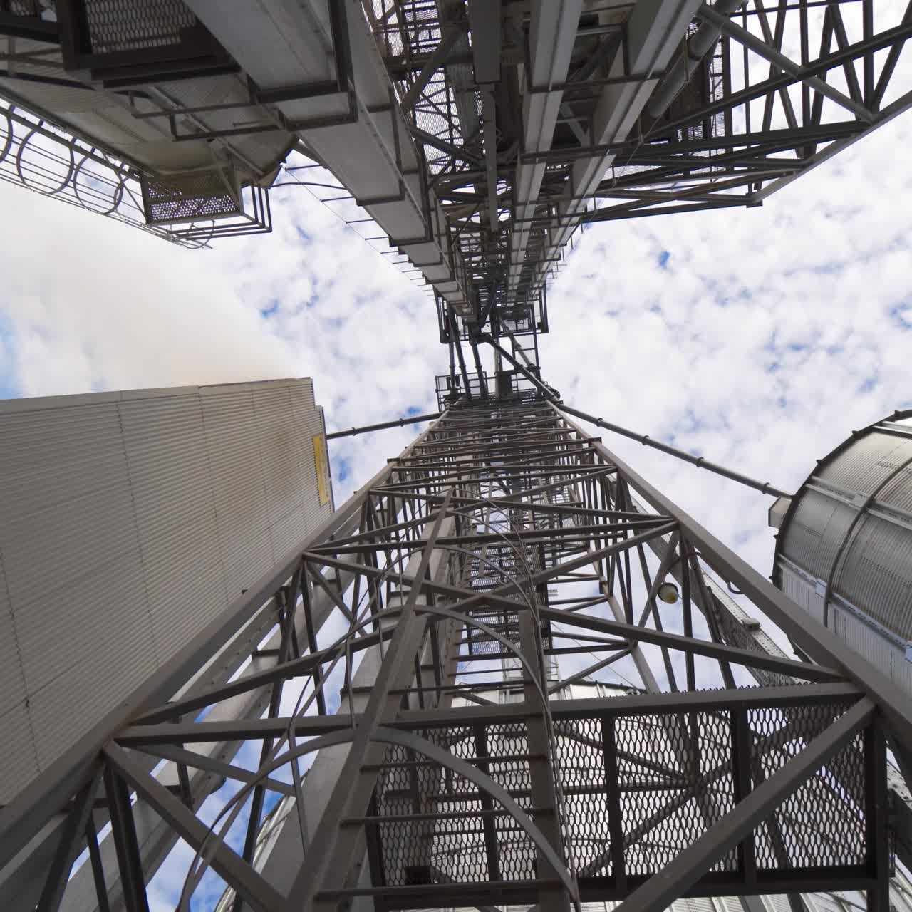Metal towers on industrial plant. Steel construction on a modern agricultural factory with grain elevators on sky background. View from below