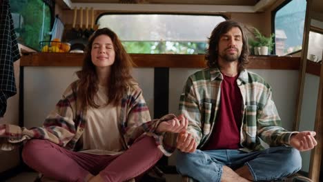 Retrato-De-Una-Pareja-Meditando,-Una-Chica-Morena-Con-Una-Camisa-A-Cuadros-Y-Pantalones-Rosas-Junto-Con-Su-Novio-Con-Una-Camisa-A-Cuadros-Verde-Y-Una-Camiseta-Roja-Sentados-En-La-Posición-De-Loto-Y-Meditando-En-Su-Casa-De-Campo-O-Remolque-Durante-Su-Picnic-Fuera-De-La-Ciudad-En-El-Verano.