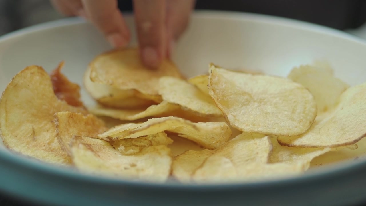 Hand Picking a Crispy Potato Chip from a Bowl