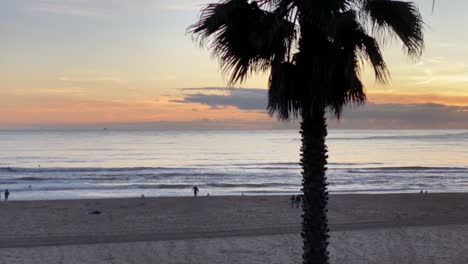 Local-surfers-running-along-beach-during-sunset-with-small-waves-crashing-with-amazing-sunset