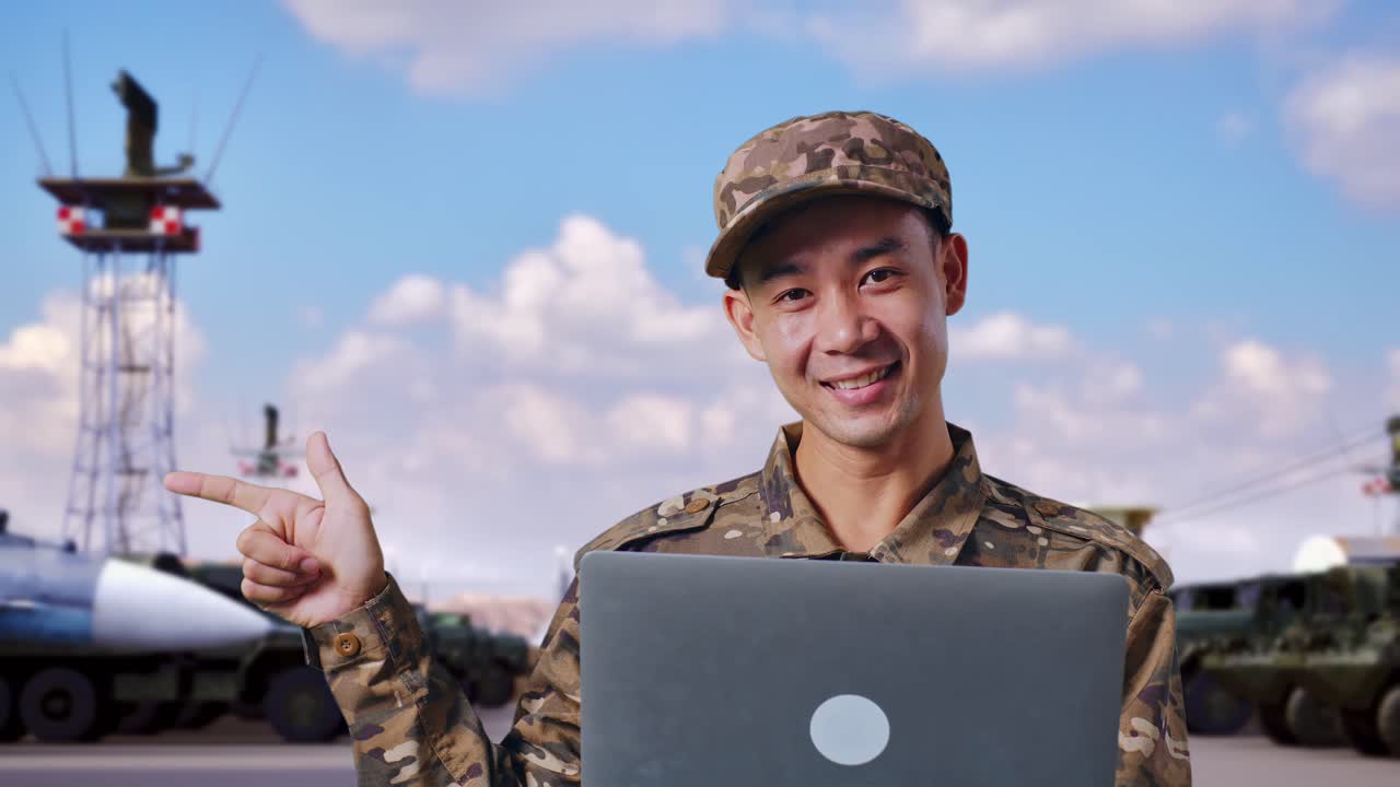 아시안 남성 군인이 노트북을 사용하고 군사 캠프에 서 있는 동안 을 가리키고 있습니다.