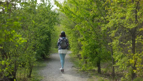 Mujer-En-E-scooter-Paseos-Por-Camino-De-Grava-A-Través-De-Arbustos-Verdes