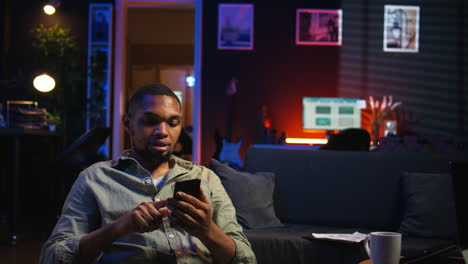 vertical video african american young guy enjoying break with his phone on sofa