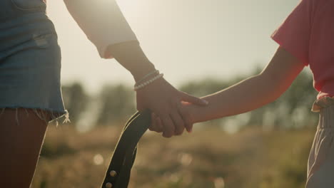 close-up of child and adult holding hands while holding rope together, adult wears pearl bracelet, and background features blurred view of vast farmland under warm sunlight