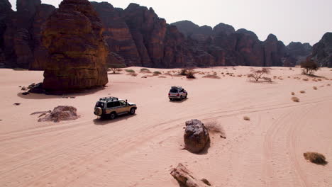 off-road suv's driving through the desert along the sandstone formation in tassili n'ajjer national park, algeria