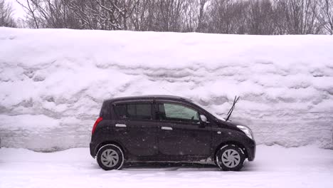 Coche-Pequeño-Estacionado-Contra-Una-Imponente-Pared-De-Nieve-En-Un-Paisaje-Invernal