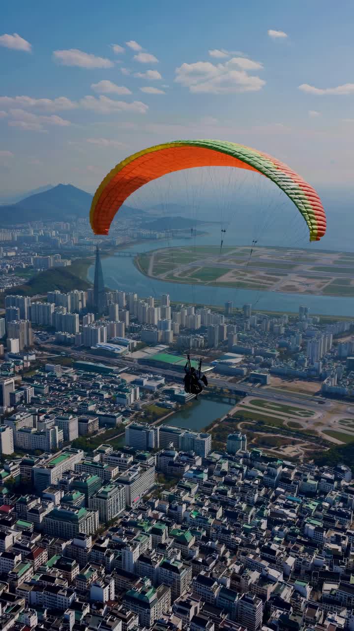 Aerial view of a paraglider soaring over a cityscape, capturing urban sprawl and distant mountains