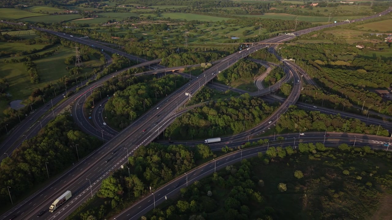 Zobacz z lotu ptaka ogromny węzeł autostradowy tętniący życiem samochodami i ciężarówkami. Pojazdy poruszają się po wielu pasach i rampach przez bujny zielony krajobraz w świetle dziennym.